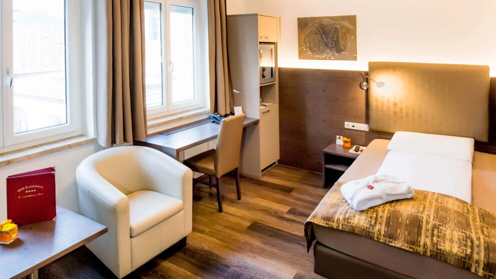 Das Business-Einzelzimmer mit Holzboden, Boxspringbett und Schreibtisch mit Blick auf den Garten im Hotel Der Kaiserhof