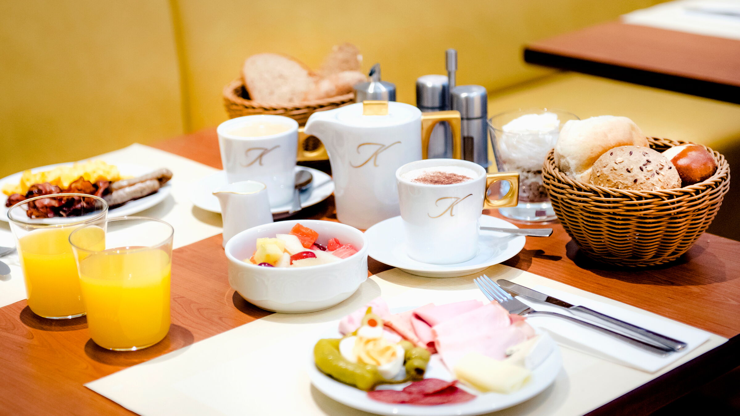 A laid breakfast table with fruit, coffee, orange juice, pastries and cold cuts.