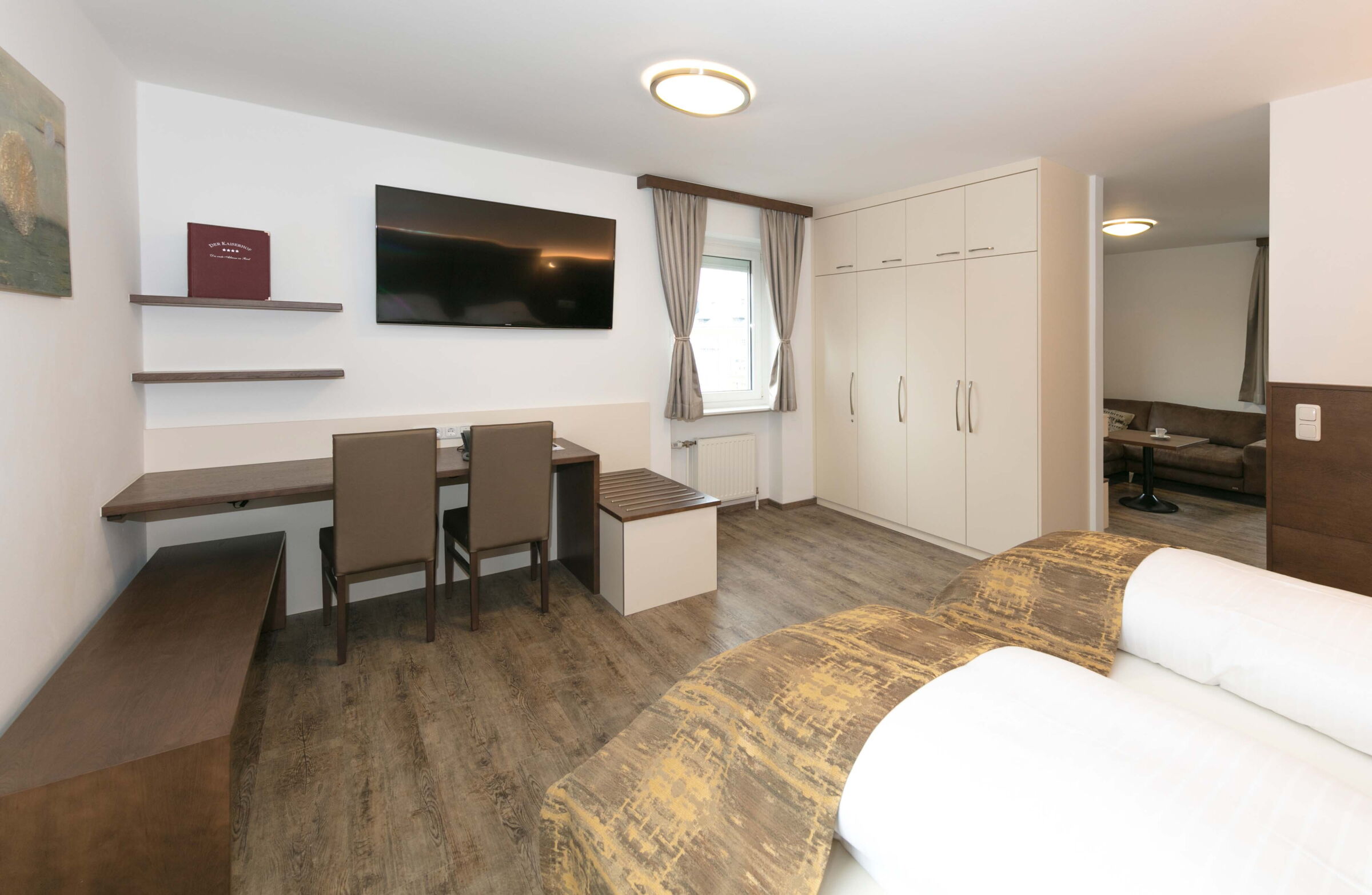 Das Schlafzimmer der Junior Suite mit einem Boxspringbett, einem Schreibtisch und Blick auf den Garten