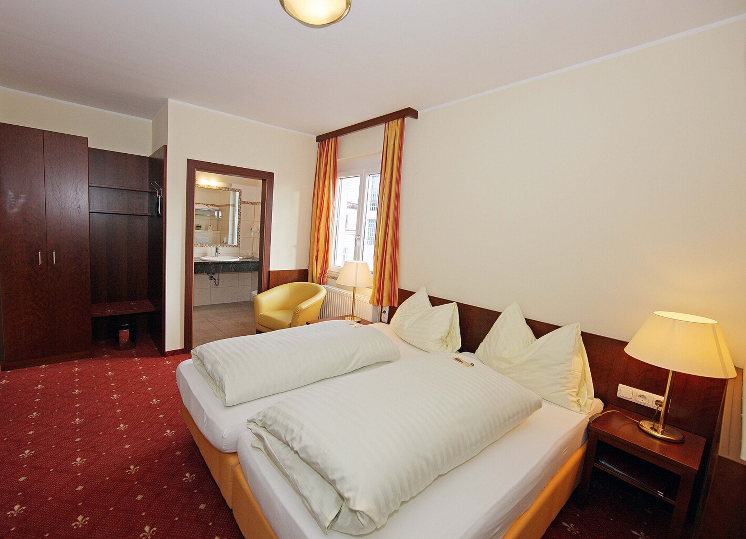 The Classic double room at Hotel Der Kaiserhof is decorated in bold colors and features a box-spring bed and red carpeting.