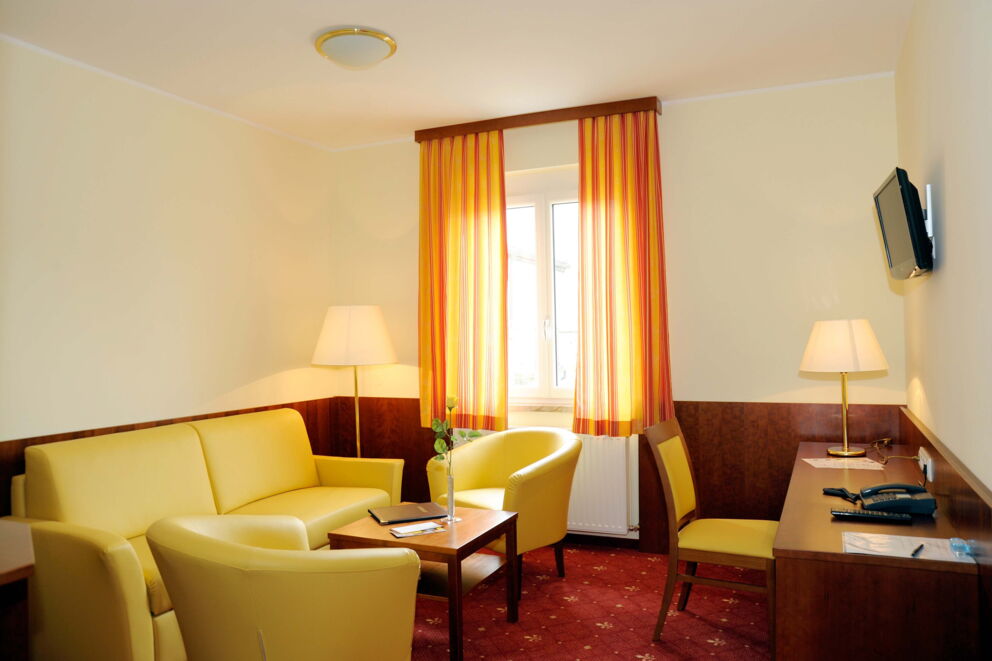 A spacious living area with a beautiful yellow couch and armchairs as well as a desk and TV in the Classic Suite at Hotel Der Kaiserhof