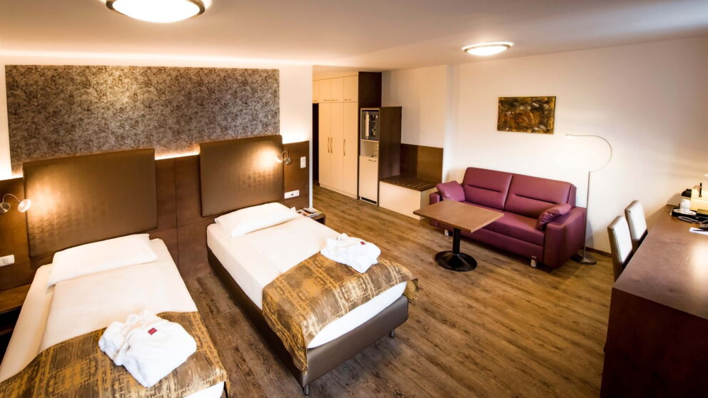 Die geräumige Junior-Suite mit zwei Boxspringbetten und einer roten Couch